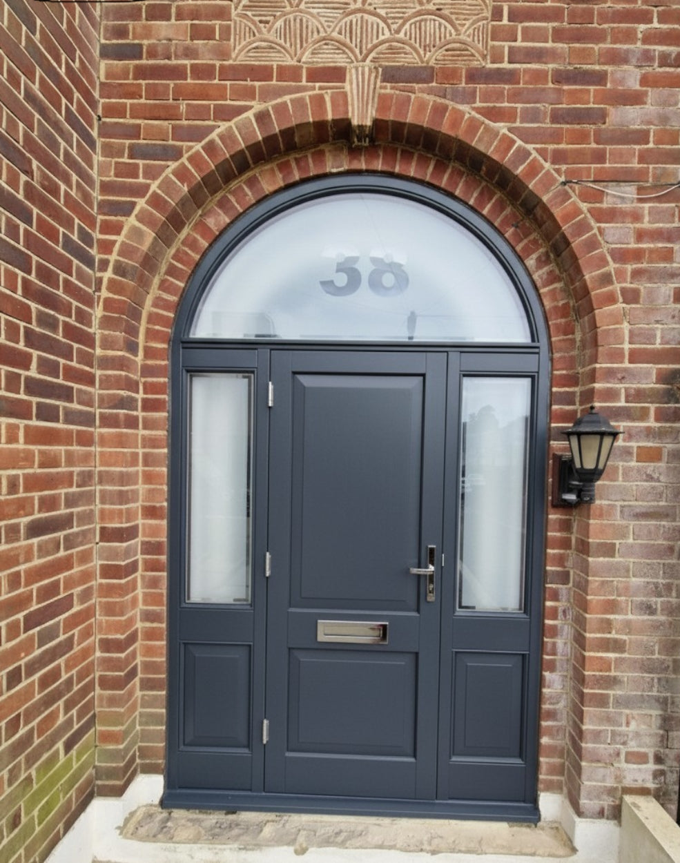 A modern dark grey  front door with an arched semi-circular glass transom window above