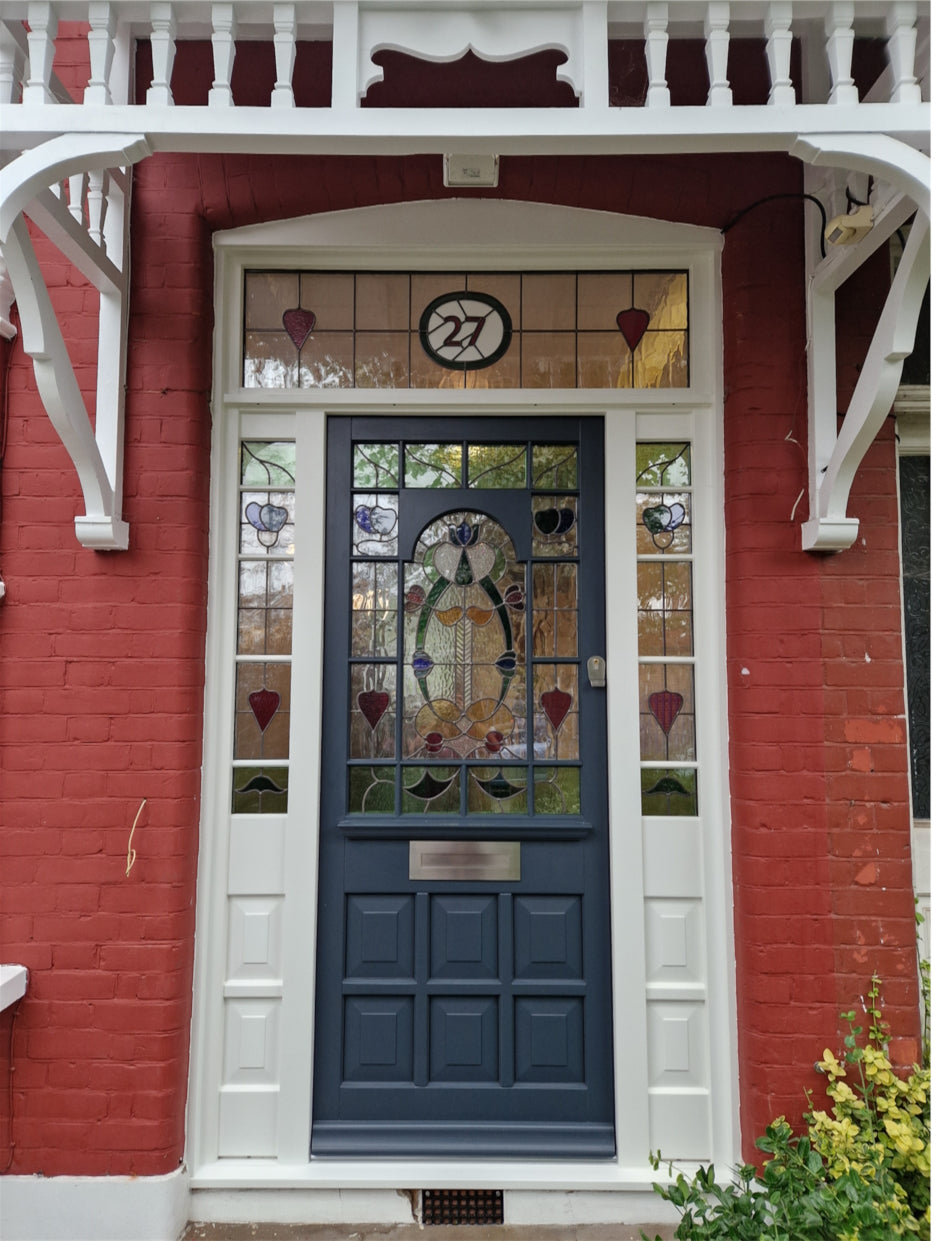 A dark blue bespoke timbere front door with a decorative stained glass panel, set within a white door frame on a red brick house exterior.