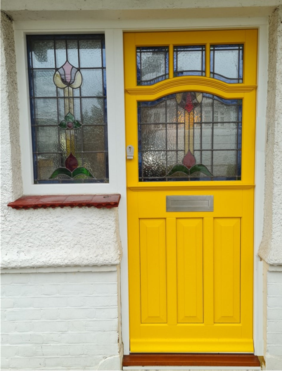 A bright yellow front door with a decorative stained glass window and a matching yellow door frame, set into a white textured wall next to a matching window.